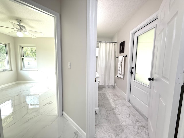 corridor with marble finish floor, a textured ceiling, and baseboards