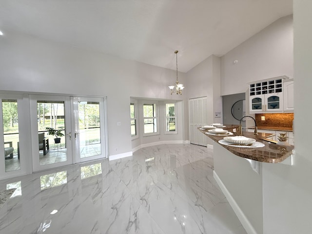 kitchen with baseboards, high vaulted ceiling, white cabinetry, a notable chandelier, and marble finish floor