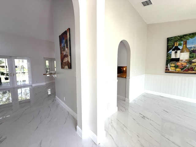 hallway with arched walkways, visible vents, marble finish floor, and french doors