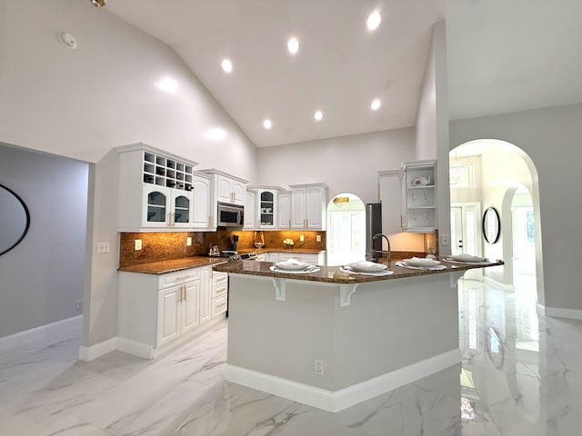 kitchen featuring marble finish floor, open shelves, stainless steel microwave, arched walkways, and a peninsula