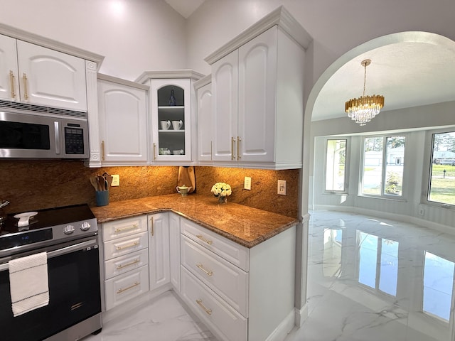 kitchen featuring arched walkways, marble finish floor, appliances with stainless steel finishes, and dark stone countertops