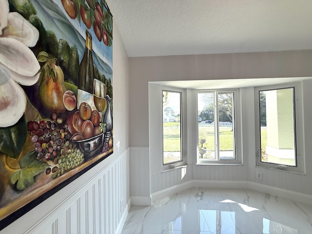 interior space with a wainscoted wall, baseboards, marble finish floor, and a textured ceiling