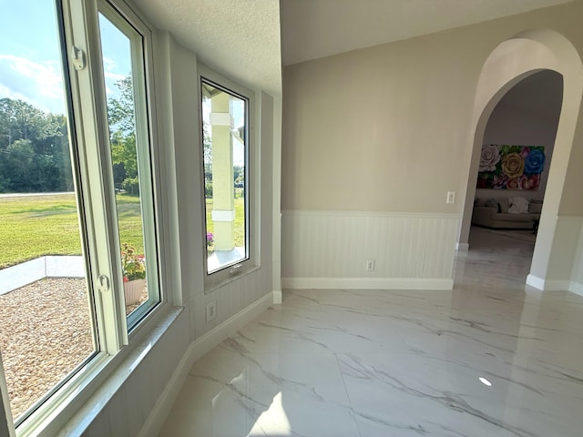 unfurnished room with baseboards, a wainscoted wall, arched walkways, marble finish floor, and a textured ceiling