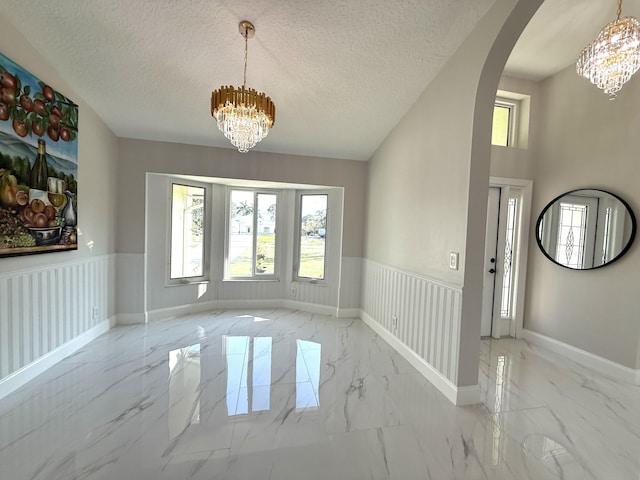 entrance foyer with marble finish floor, an inviting chandelier, and wainscoting