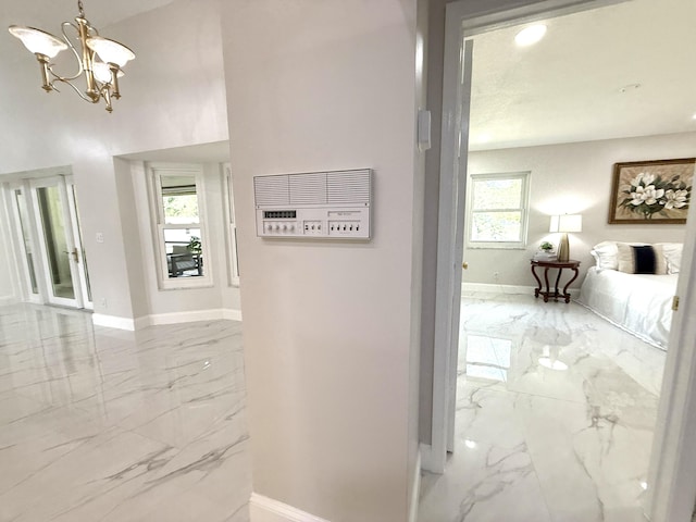 hallway with marble finish floor, baseboards, and an inviting chandelier