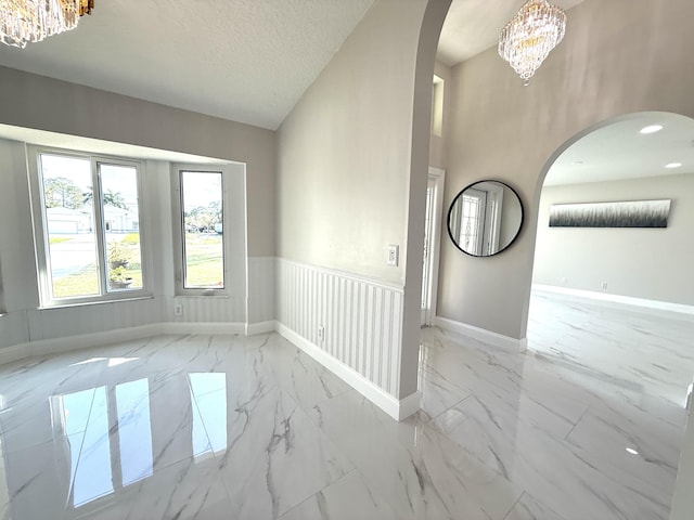 spare room with arched walkways, a notable chandelier, marble finish floor, and a textured ceiling