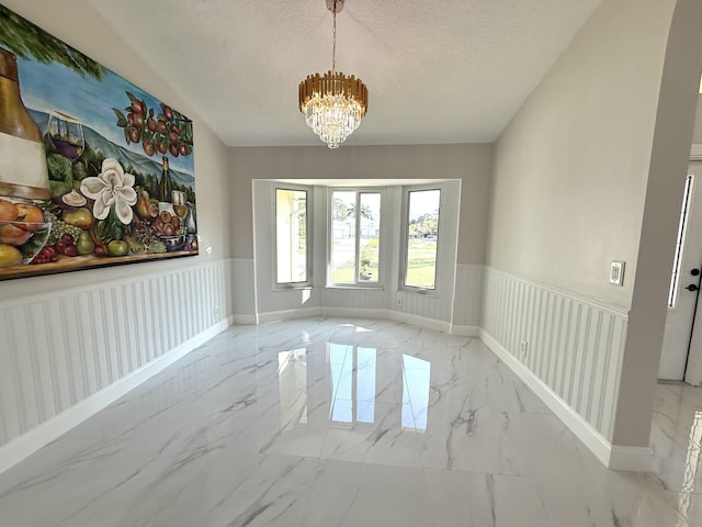 interior space featuring a wainscoted wall, a textured ceiling, marble finish floor, and an inviting chandelier