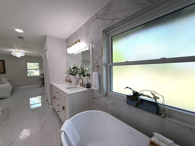 bathroom with a sink, a freestanding bath, marble finish floor, and a textured ceiling