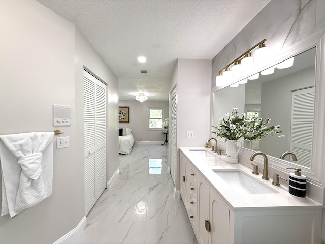 ensuite bathroom with marble finish floor, ensuite bathroom, a sink, a textured ceiling, and baseboards