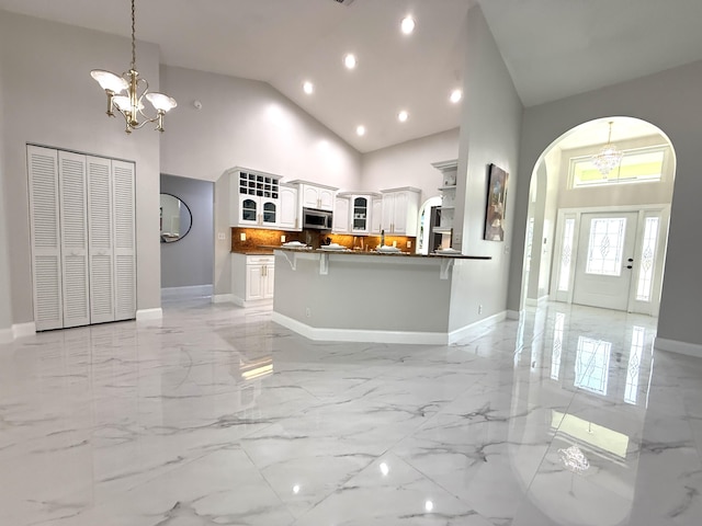 kitchen with stainless steel microwave, glass insert cabinets, an inviting chandelier, arched walkways, and marble finish floor