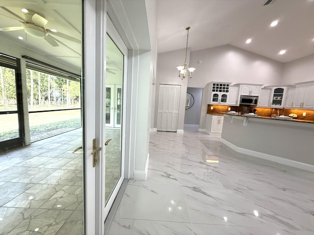 kitchen with glass insert cabinets, stainless steel microwave, ceiling fan with notable chandelier, and marble finish floor