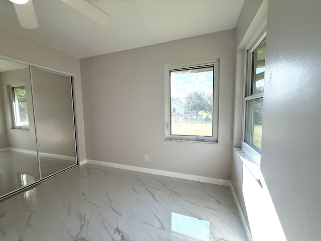 unfurnished bedroom with a closet, multiple windows, marble finish floor, and baseboards