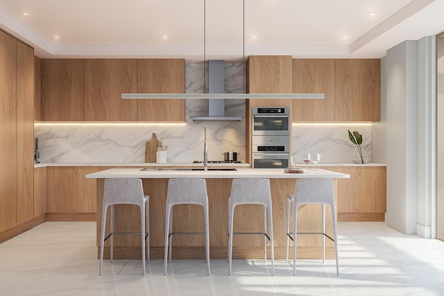 kitchen with a kitchen island with sink, stainless steel double oven, a breakfast bar area, wall chimney range hood, and tasteful backsplash