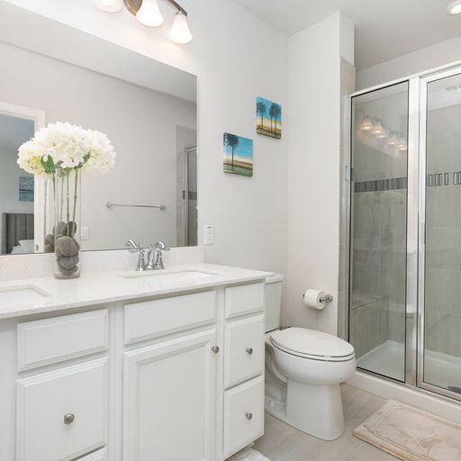 bathroom featuring a shower with door, tile flooring, dual vanity, and toilet