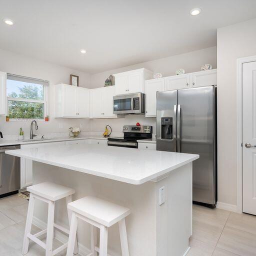 kitchen with white cabinetry, appliances with stainless steel finishes, a breakfast bar, sink, and a kitchen island