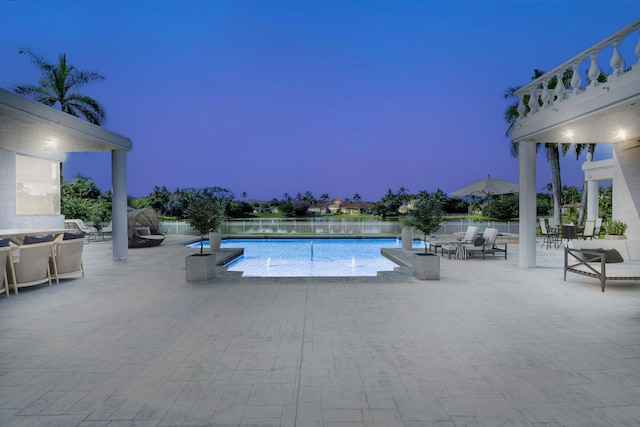 pool at dusk featuring a patio and a water view