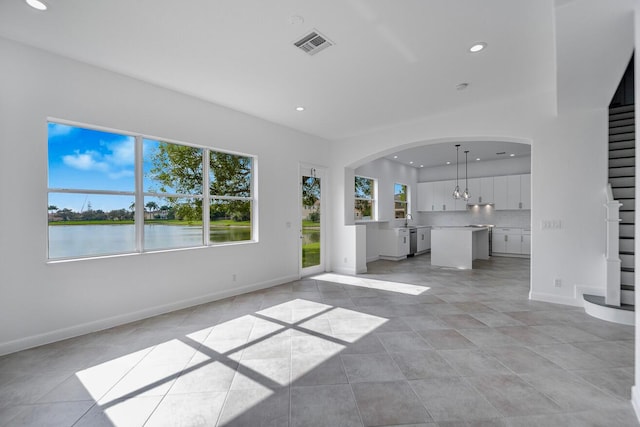 unfurnished living room with a water view, light tile flooring, sink, and a notable chandelier