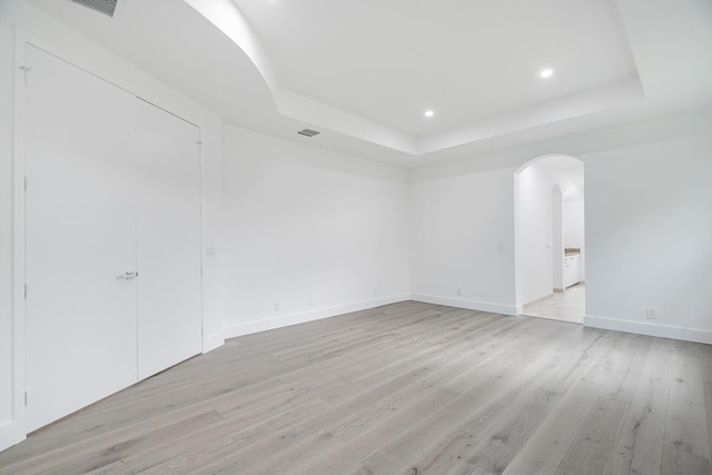 empty room featuring a raised ceiling and light hardwood / wood-style flooring