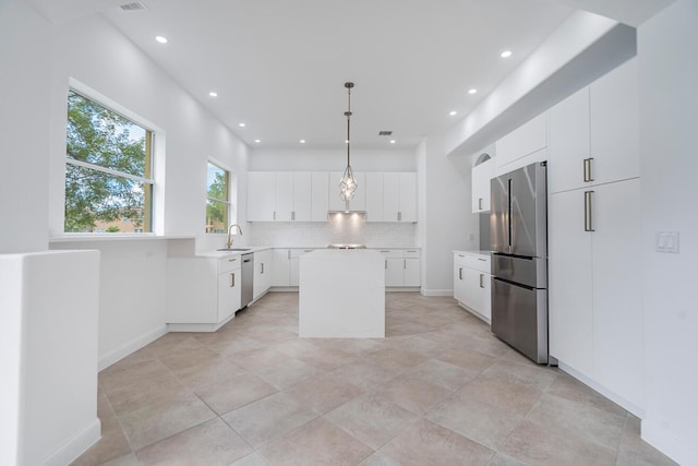 kitchen featuring appliances with stainless steel finishes, light tile floors, white cabinets, a kitchen island, and tasteful backsplash