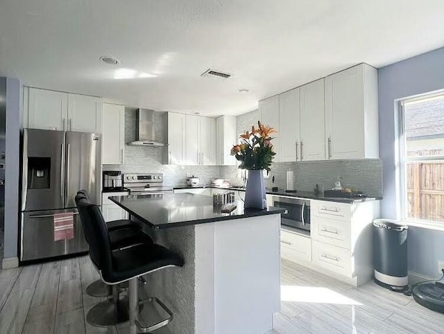 kitchen featuring white cabinetry, stainless steel appliances, a center island, and wall chimney exhaust hood