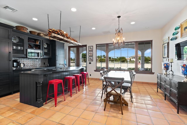 kitchen featuring an island with sink, hanging light fixtures, tasteful backsplash, and a chandelier