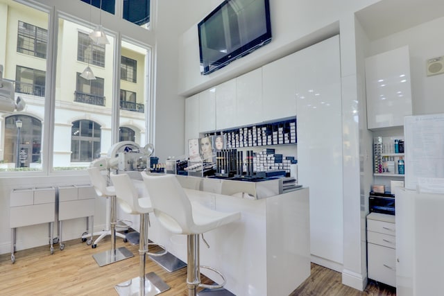 bar with a towering ceiling, hanging light fixtures, white cabinets, and light wood-type flooring