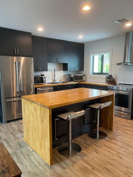 kitchen featuring appliances with stainless steel finishes, a center island, light hardwood / wood-style flooring, and wall chimney range hood