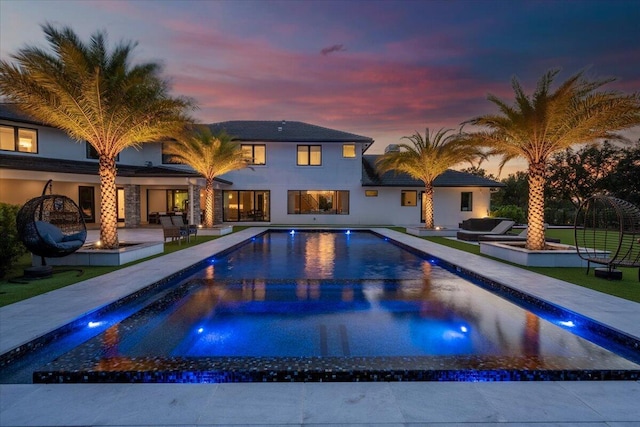 pool at dusk featuring a patio and a yard