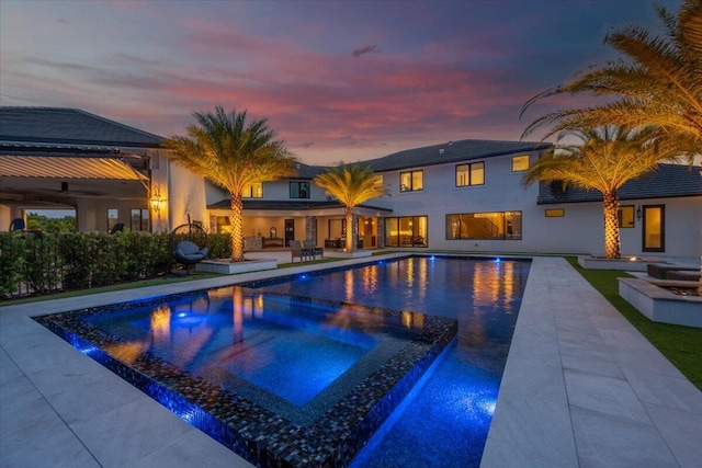 pool at dusk featuring an in ground hot tub and a patio area