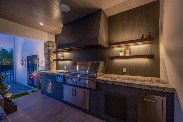 kitchen featuring dark hardwood / wood-style floors, light stone countertops, dark brown cabinets, and wall chimney exhaust hood