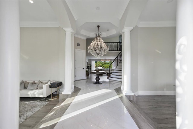 foyer entrance with a notable chandelier, ornamental molding, a raised ceiling, decorative columns, and light wood-type flooring