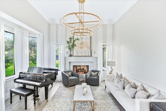 living area with a chandelier, a high ceiling, a high end fireplace, and light hardwood / wood-style flooring