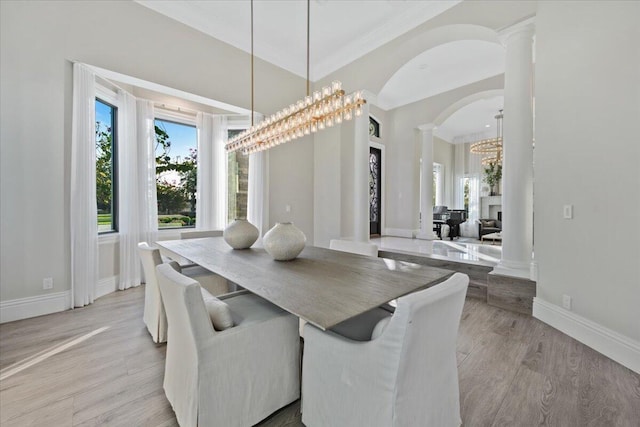 dining area featuring a chandelier, a fireplace, crown molding, light wood-type flooring, and ornate columns