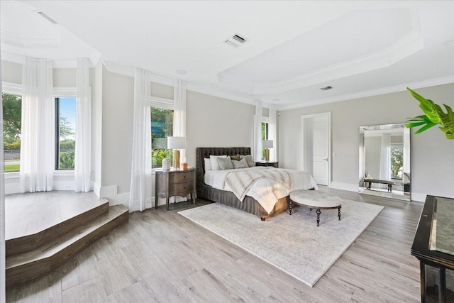 bedroom with ornamental molding, a tray ceiling, and light wood-type flooring