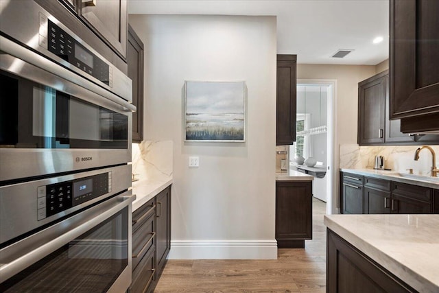 kitchen featuring double oven, light hardwood / wood-style floors, tasteful backsplash, dark brown cabinets, and sink