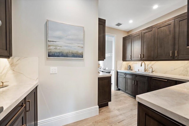 kitchen with dark brown cabinetry, tasteful backsplash, light hardwood / wood-style floors, and sink