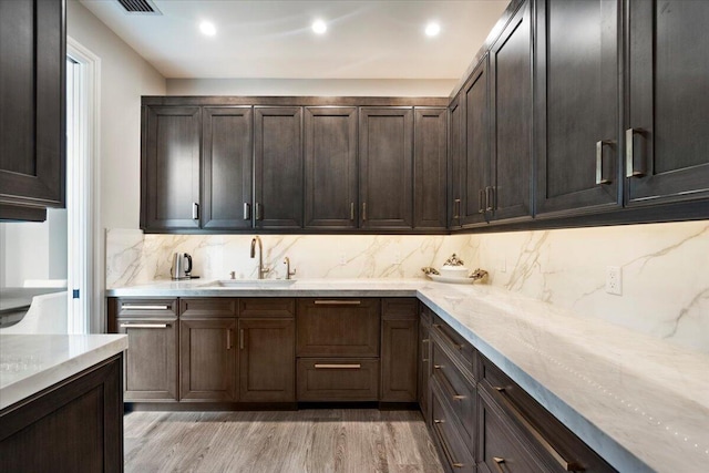 kitchen with light stone countertops, light hardwood / wood-style floors, sink, tasteful backsplash, and dark brown cabinetry