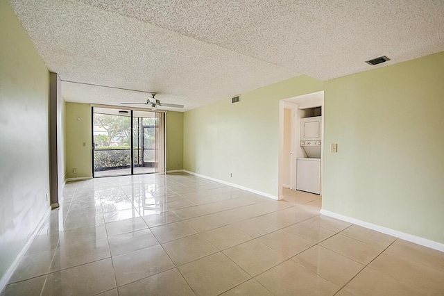 unfurnished room featuring a textured ceiling, expansive windows, ceiling fan, and stacked washer and clothes dryer