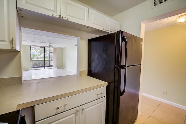 kitchen with ceiling fan, light tile floors, black refrigerator, white cabinets, and a textured ceiling