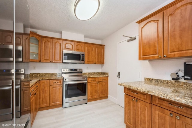 kitchen with light stone counters, stainless steel appliances, light hardwood / wood-style floors, and a textured ceiling