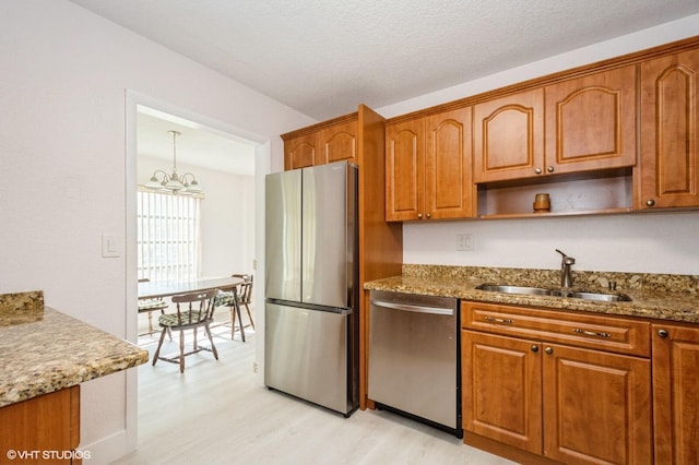 kitchen featuring sink, stone counters, stainless steel appliances, decorative light fixtures, and light wood-type flooring