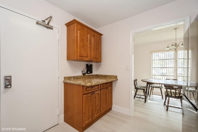 kitchen with an inviting chandelier, light stone counters, pendant lighting, and light hardwood / wood-style floors