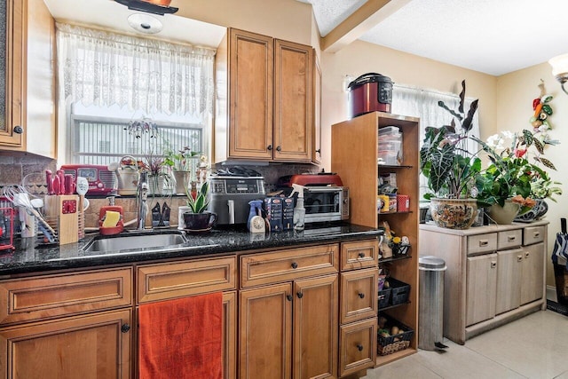 kitchen featuring backsplash, sink, light tile floors, and dark stone counters