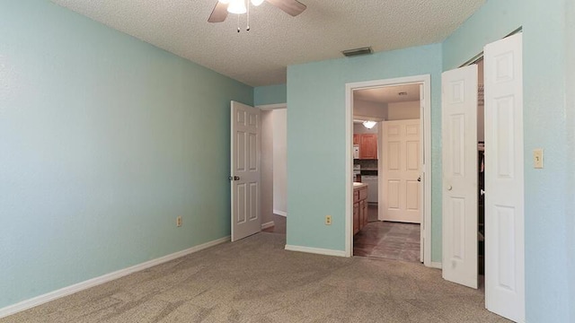 unfurnished bedroom with a textured ceiling, dark colored carpet, ceiling fan, and ensuite bathroom