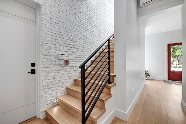 stairway featuring a wall mounted air conditioner, light hardwood / wood-style floors, and brick wall