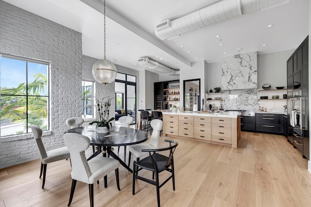 dining space with a high ceiling, brick wall, and light hardwood / wood-style flooring