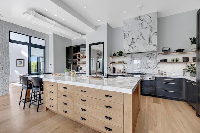 kitchen featuring a center island with sink, light brown cabinetry, light hardwood / wood-style flooring, and a breakfast bar area