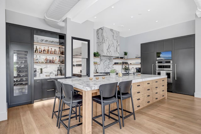 kitchen featuring a kitchen island with sink, a breakfast bar area, light hardwood / wood-style floors, double oven, and light stone countertops