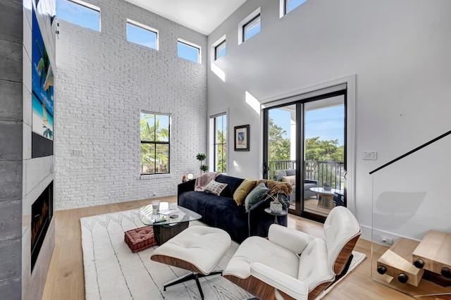 living room with brick wall, plenty of natural light, light hardwood / wood-style floors, and a towering ceiling