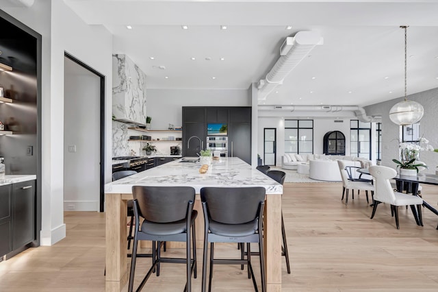 kitchen with an island with sink, light hardwood / wood-style floors, decorative light fixtures, a breakfast bar area, and sink